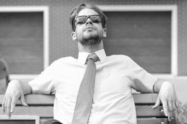 Emlakçı bankta oturur ve iş günü sonra rahatla. Şehir sokak güneş gözlüğü takıyor yukarı seyir yetişkin iş adamı