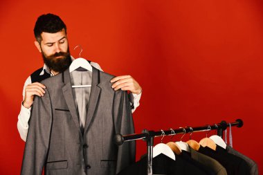 Sakallı hippi adam elbise ile rafın yanında duruyor.