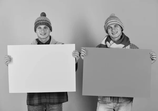 Irmãos gêmeos em chapéus quentes e cachecóis segurar placas amarelas e laranja, espaço de cópia. Os irmãos apresentam a venda de outono. Homens com rostos sorridentes felizes — Fotografia de Stock