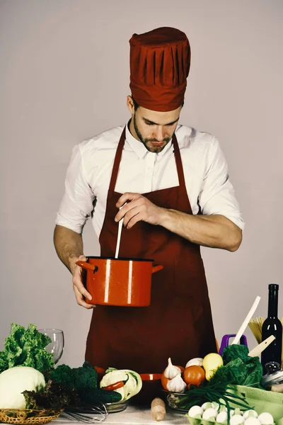 Küche und professionelles Kochkonzept. Koch mit geschäftigem Gesicht hält roten Topf auf grauem Hintergrund. — Stockfoto