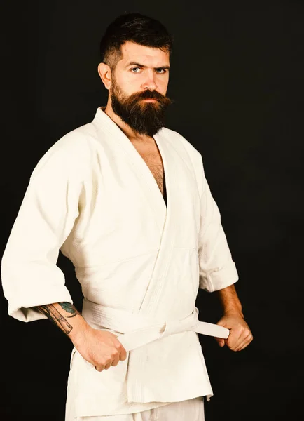Karate man with serious and confident face in uniform. Man with beard in white kimono on black background.