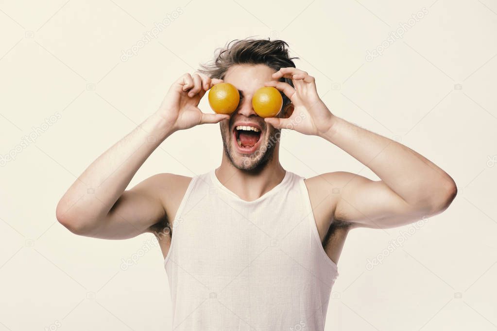 Guy with happy face isolated on light grey background. Man with oranges instead of eyes in his hands