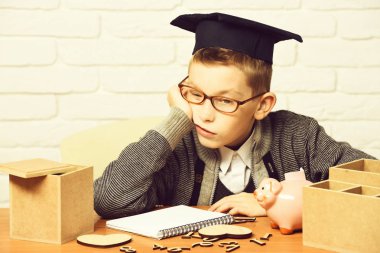 gri kazak ve masada oturan gözlük yandan boşaltmak ahşap numaraları pembe domuz domuz banka sınıf mezuniyet şapkalı beyaz tuğla duvar zemin üzerine eğildi