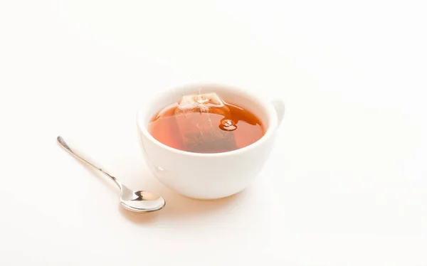 Tazza riempita con acqua calda e sacchetto intinto di tè nero. Processo di preparazione del tè nero in tazza di ceramica. Concetto di tè. Tazza riempita con acqua bollente, bustina di tè e cucchiaio su sfondo bianco — Foto Stock