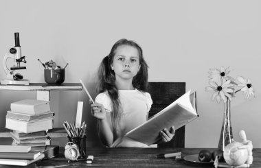 Kız ciddi bir yüz ile kitap ve mavi kalem tutar. Kız öğrenci masada ciddi yüzle oturur.