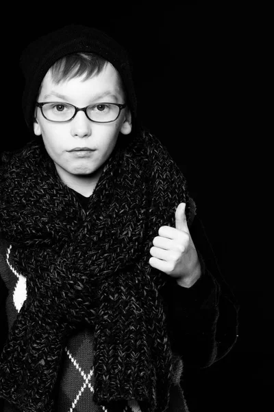 小男孩或可爱的书呆子，戴着眼镜，头戴帽子，头戴黑色背景的时髦针织围巾，竖起大拇指, — 图库照片
