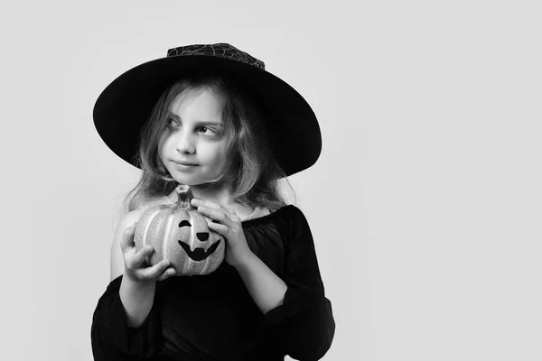 Chica con calabaza naranja tallada aislada sobre un fondo amarillo cálido, espacio para copiar. Niño disfrazado de bruja y gato o linterna — Foto de Stock