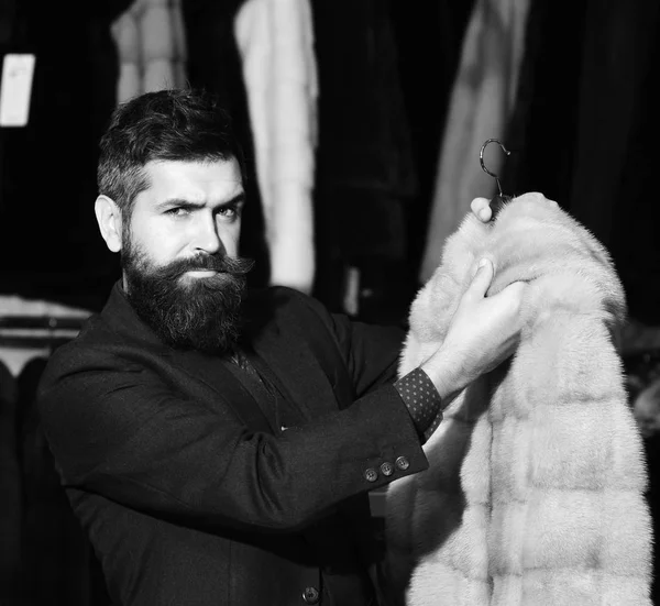 Macho με κομψή εμφάνιση με γούνα βιζόν σε κατάστημα μόδας. Άνδρας με μούσι και μουστάκι κατέχει γούνινο παλτό. — Φωτογραφία Αρχείου