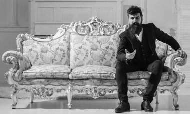 Maço çekici ve zarif ciddi bir yüz ve düşünceli ifade. Moda ve stil kavramı. Adam sakal ve bıyık moda klasik takım elbise ile eski moda koltuk ya da kanepe üzerinde oturur.