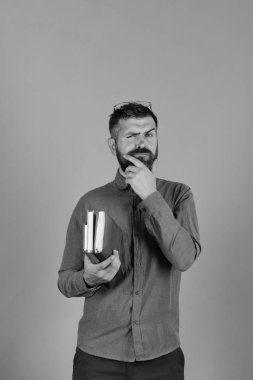 Düşünceli yüz ve sakal tutar yığın kitap mavi arka plan üzerinde olan adam.