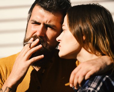 Erkek ve kadın defocused beyaz çizgili arka planda ciddi yüzlerle. Kız ve sakallı adam sarılmak ve sigara tutun