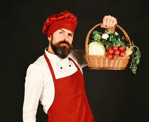 Koch mit Kohl, Rettich, Pfeffer und Salat. Koch mit ernstem Gesicht in weinroter Uniform hält Gemüse in der Hand — Stockfoto