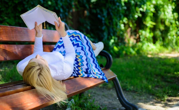 Time for self improvement. Woman spend leisure with book. Lady enjoy reading. Girl reading outdoors while relaxing on bench. Girl lay bench park relaxing with book, green nature background