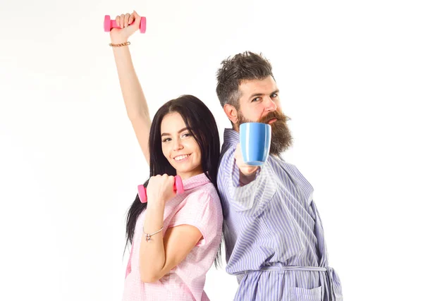 Fille avec haltère, homme avec tasse de café. Couple, famille au visage endormi, pleine d'énergie. Couple amoureux en pyjama, peignoir isolé sur fond blanc. Concept alternatif du matin — Photo