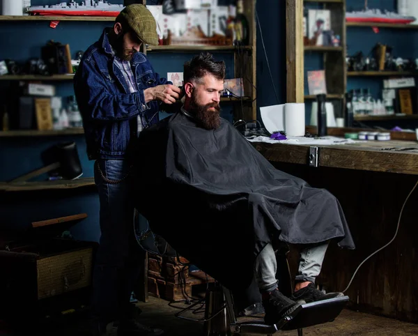 Barber with clipper trimming hair on nape of client. Hipster client getting haircut. Hipster style concept. Barber with hair clipper works on haircut of bearded guy barbershop background