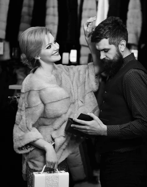 Casal apaixonado tenta sobretudos caros, cara com barba e mulher comprar casaco peludo . — Fotografia de Stock