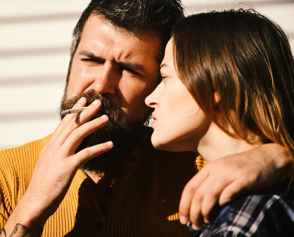 Homem e mulher com rostos sérios no fundo listrado branco, desfocados. Menina e barbudo cara abraçar e segurar cigarro — Fotografia de Stock