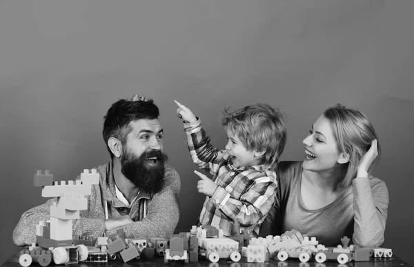 Familia con caras felices construir coches de juguete de bloques de construcción de colores. La paternidad y el concepto de juego. Hombre con barba, mujer y niño — Foto de Stock