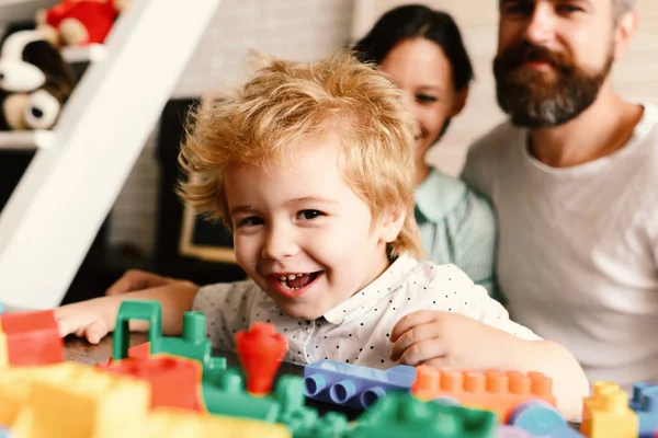 Parents and son with happy faces make brick construction. Young family spends time in playroom. Mom and dad