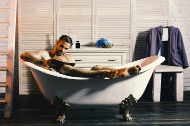 Küvet ve okuma kitapta çıplak oturan maço. Adam sakal ve konsantre yüz okuma kitabı