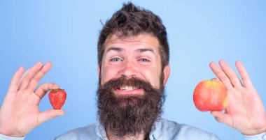 Yaz aylarında faydaları. Sakallı adam gülen elma ve çilek eller mavi arka planda tutar. Vitamini meyve beslenme kavramı. Vitamini diyet sağlık. Meyve ve meyve eller sağlıklı alternatif
