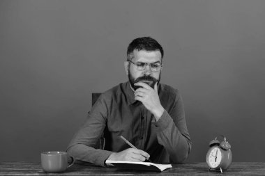 Kupası, retro saat ve vintage masada kırmızı kitap. Sakal, gözlük yazıyor defterde kırmızı zemin üzerine adamım