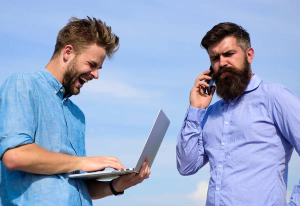 Business team works outdoor, sky background. Men with laptop and smartphone solving problems using mobile internet. Workers with gadgets always having access to mobile internet. Always online