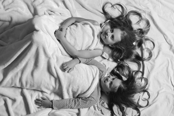 Les filles s'allongent sur fond de draps blancs et roses. Enfants avec des visages heureux et des coeurs dans les cheveux au lit — Photo