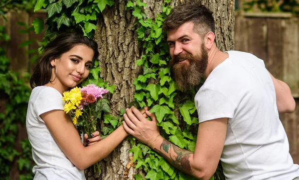 Pareja enamorada cita romántica paseo naturaleza árbol fondo. Fecha agradable en el entorno de la naturaleza. Hombre barbudo hipster sostiene la mano novia. Pareja enamorada apoyada en el maletero con hiedra. Unidos con la naturaleza — Foto de Stock