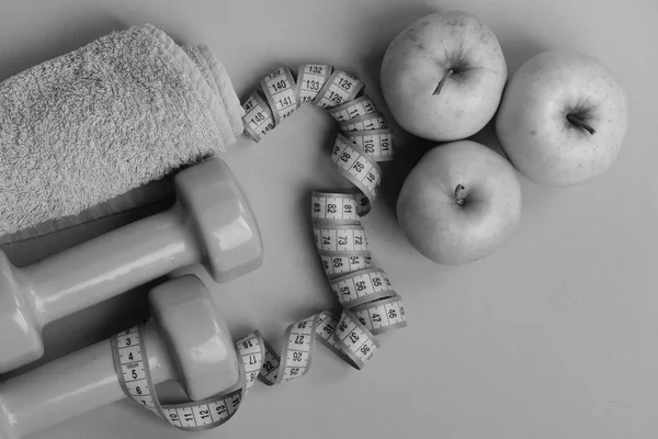 Athletics and weightloss concept. Dumbbells in bright green color, twisted measure tape, towel, fruit