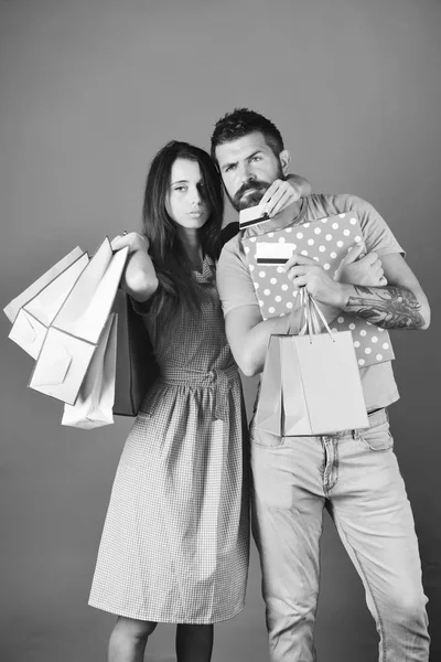Man met baard houdt creditcard en vak. Paar houdt boodschappentassen op blauwe achtergrond en knuffels. — Stockfoto