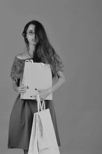 Girl with smart glasses and interested face, copy space. Lady stands on yellow background, holds pink shopping bags. — Stock Photo, Image