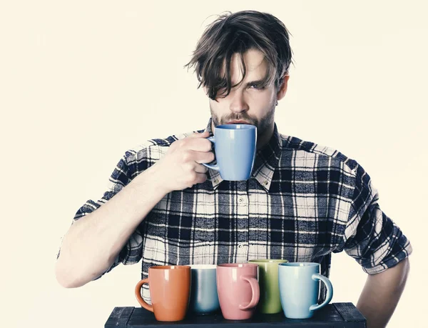 Beau barbu en noir et blanc chemise à carreaux avec cheveux échevelés sérieux face plateau de maintien avec des tasses colorées et boire isolé sur fond blanc, espace de copie . — Photo