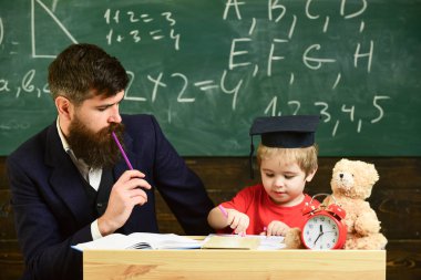 Hometask kavramı. Hometask, çocuk, yardımcı olur kontrol baba evlat. Öğretmen formal giyim ve öğrenci sınıfta kolej, kara tahta arka plan. Hevesli çocuk öğretmen ile eğitim