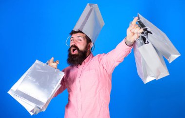 Satış sezon indirimlerle alışveriş adam. Kafasında torba ile neşeli yüzündeki hipster bağımlısı Alışverişkoliğin var. Adam sakal ve bıyık taşır alışveriş torbaları, mavi arka plan ile. Alışveriş kavramı