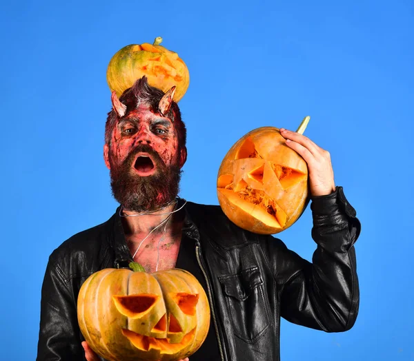 Demon with horns and proud face holds carved jack lanterns