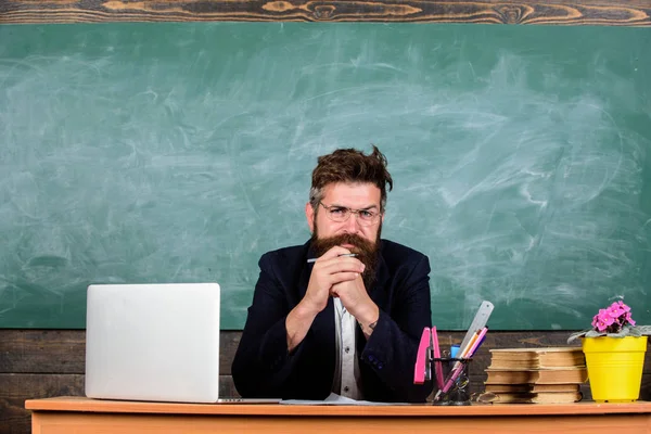 Вчитель бородатий зрілий шкільний вчитель слухає з увагою. Формальний одяг вчителя сидить на фоні класної дошки столу. Вчитель слухає відповідь або звіт. Зверніть увагу на подробиці — стокове фото