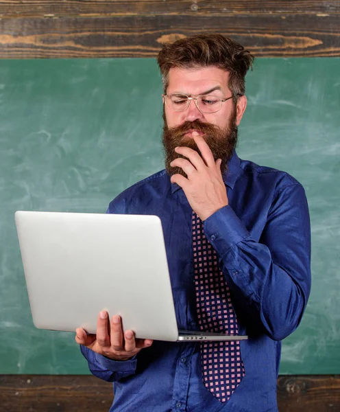 Concepto de educación a distancia. Navegar por Internet. Hipster profesor usar gafas y corbata sostiene portátil navegar por Internet. Profesor barbudo hombre con portátil moderno navegar por internet pizarra fondo —  Fotos de Stock