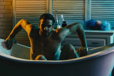 Güçlü kolları olan, küvette çıplak oturan maço. 