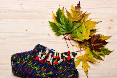 Sonbahar düşen yapraklar, kalpleri ve ışık arka plan üzerinde örme eşarp ile küçük iğneler. Sonbahar sezonu kavramı. Doğal ahşap zemin üzerine kurutulmuş akçaağaç yaprağı. Renkli ahşap dokusu üzerinde yaprak