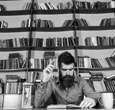 Adam meşgul yüz kitap okumak, kitap rafı arka plan üzerinde. Eğitim ve bilim kavramı. Bilim adamı okuma, kupa ve kum saati ile masada oturur. Öğretmen ya da sakal Kitaplığı'nda eğitim ile öğrenci