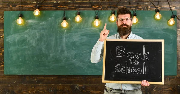Vissza ehhez: iskola fogalmát. A szemüvegek tanár tartja tábla, felirat vissza az iskolába. Férfi szakáll és bajusz, a szigorú arcát figyelmeztet diákok, chalkboard háttér — Stock Fotó