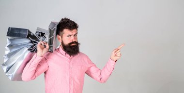 Satış ve indirim kavramı. Parmak ile işaret alışveriş satış sezonu üzerinde adam. Ciddi yüz hipster Alışverişkoliğin bağımlısı. Sakal ve bıyık taşır grup alışveriş torbaları, gri arka plan ile adam