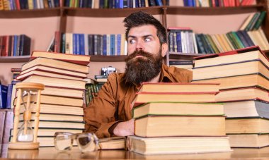 Kitap kurdu kavramı. Katı yüz sit Kitaplığı'nda, eğitim sırasında kitaplar, kitap rafı arka plan üzerinde yığınları arasında adam. Öğretmen veya tablo ile kum saati ve defocused gözlük, sakal oturup ile öğrenci