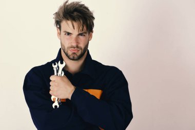 Hizmet ve inşaat kavramı. Adam üniformalı ciddi bir yüz ile anahtar araçları tutar