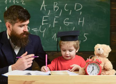 Öğretmen ve öğrenci kolej, kara tahta arka plan içinde. Çocuk çalışmaları dikkatle dinlerken öğretmen ile. İlköğretim kavramı. Baba oğul öğretir temel bilgi, tartışmak, açıklamak