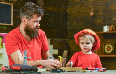 Babalık kavramı. Baba, anne-baba ile oğlu oyuncakla oynarken testere için küçük oğlu öğretim sakal gördüm. Çocuk, çocuk ile baba el testeresi kullanmayı öğrenme koruyucu kask içinde meşgul