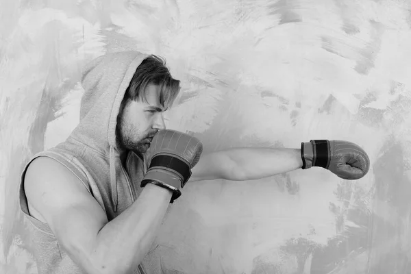 El tipo con capucha gris sin mangas usa guantes de boxeo de cuero rojo. Boxeador con trenes faciales concentrados y hace ponche —  Fotos de Stock