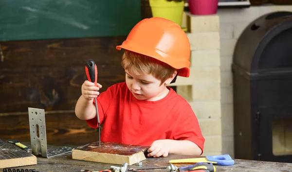 童年的概念。男孩在橙色硬帽子或头盔, 学习室背景。孩子梦想未来的建筑或建筑事业。男孩扮演建设者或修理工, 使用工具 — 图库照片