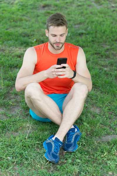 Uygulama ayarlamak. Sporcu smartphone ve pedometer ile koşu için hazır olun. Ne kadar yol uygulama kullanarak dürtmek için ayarlayın. Adam ciddi bir yüz smartphone dürtmek çim çayır arka plan başlamak için hazır tutar